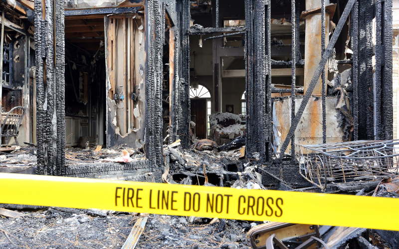 Charred remains of a building interior are seen behind yellow "Fire Line Do Not Cross" tape after a severe fire, highlighting the urgent need for professional Restoration Services.