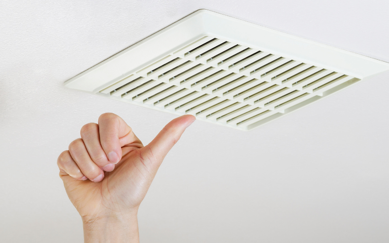 A hand gives a thumbs-up gesture near a white ceiling air vent with rectangular slats, signaling satisfaction after professional air vent cleaning.