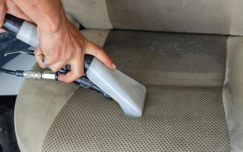 A person uses a vacuum extraction tool to clean a beige car seat, showcasing expert Restoration Services.