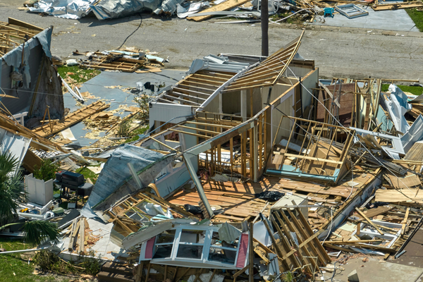 A house lies in ruins after a natural disaster, with broken walls, exposed framing, and debris scattered across the ground and nearby street, awaiting professional Restoration Services to help rebuild what was lost.