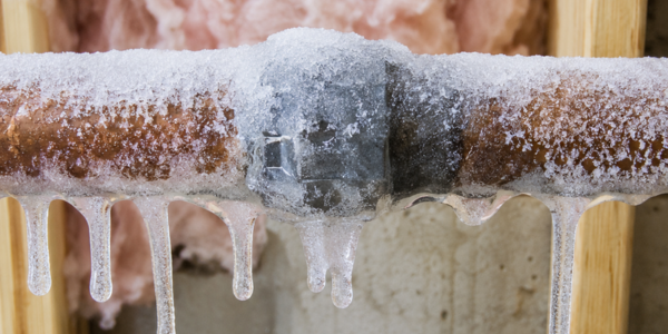 A metal pipe covered in frost and icicles, with frozen water droplets hanging from it, is shown inside a building—a clear sign that professional Water Damage or Flood Cleanup services may soon be needed if the situation isn’t addressed.