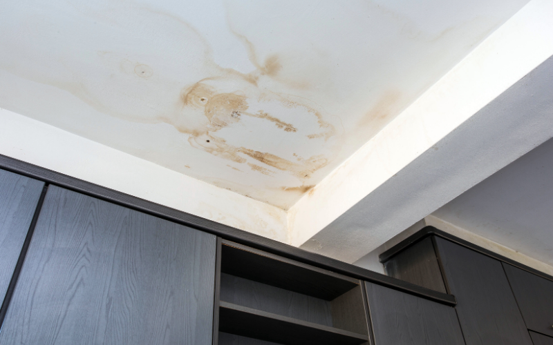 Water-stained ceiling above dark cabinets, showing discoloration and damage, likely due to a leak or moisture problem—professional Restoration Services may be needed to repair and prevent further issues.