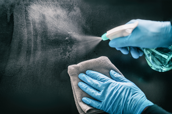 Person wearing blue gloves sprays cleaner onto a surface while holding a cloth, preparing to wipe and disinfect the area as part of professional restoration services.